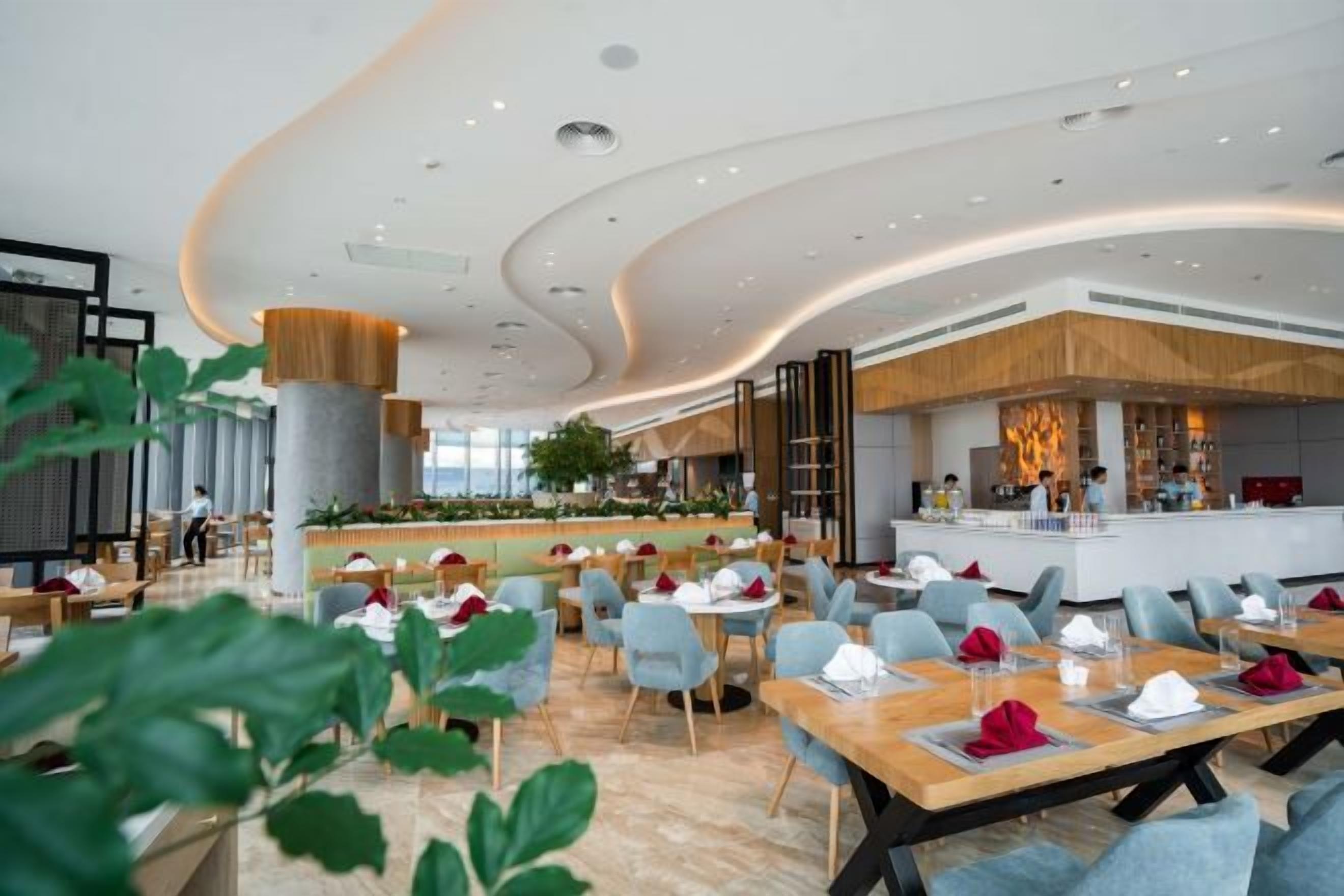 Ein modernes Restaurant mit einer zentralen Bar, verschiedenen Sitzgelegenheiten und einer sichtbaren Küche im Hintergrund.