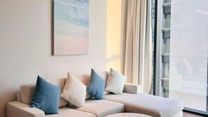 Een moderne woonkamer met een beige hoekbank, een groot raam met gordijnen en een schilderij aan de muur.