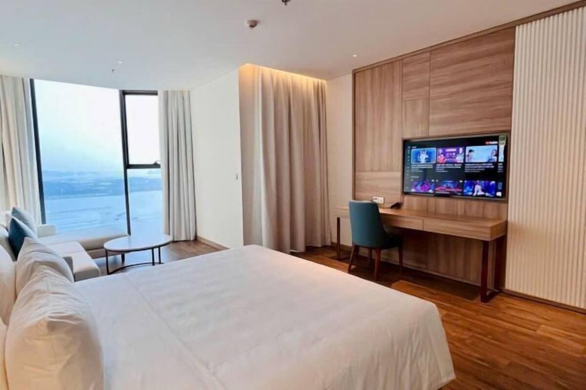 Hotelkamer met een bed, een bureau, een stoel, een televisie en een groot raam met gordijnen.