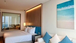 Een hotelkamer met een groot bed, een bank, een tv aan de muur en een schilderij van een strandgezicht.