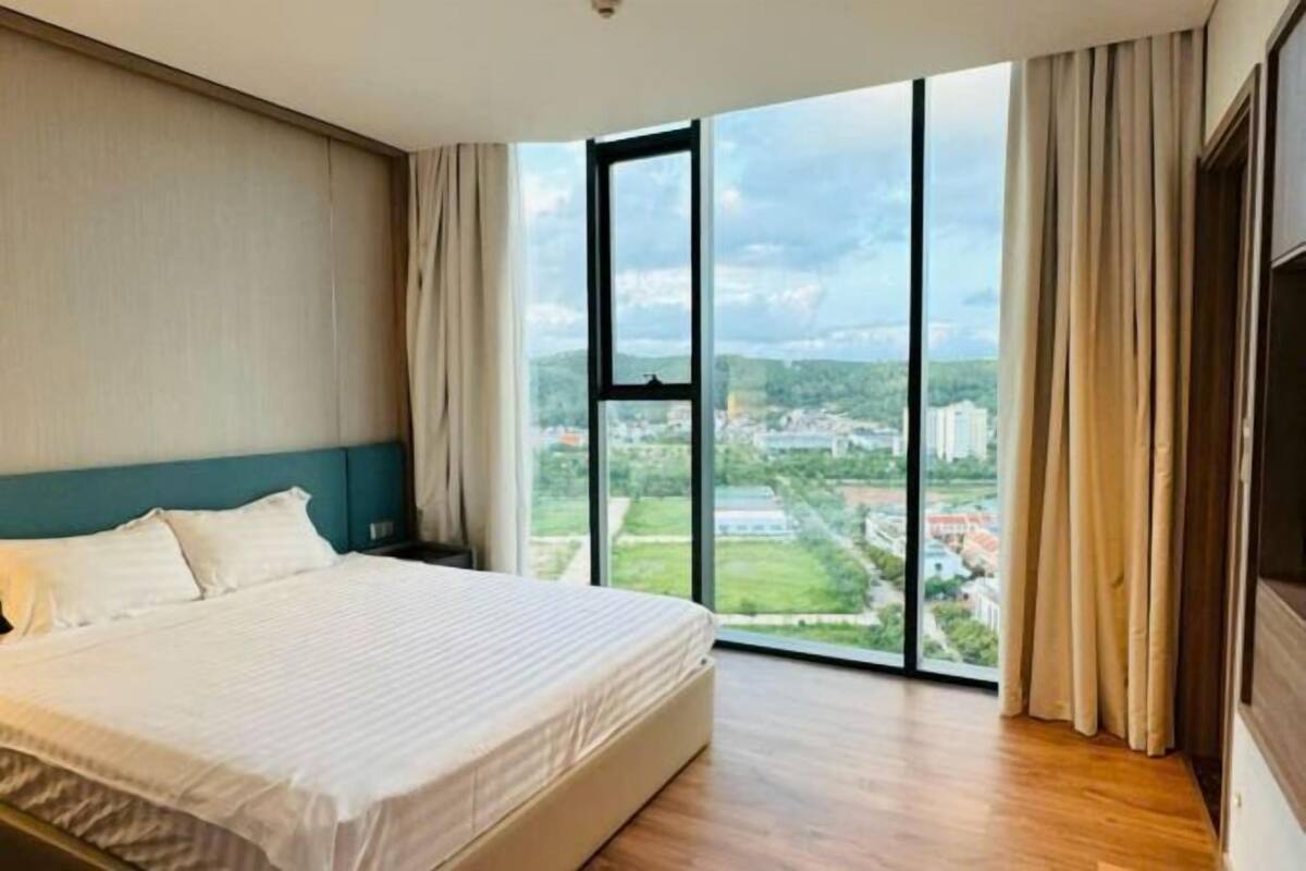 Een slaapkamer met een bed, een groot raam en uitzicht op een stadsgezicht.