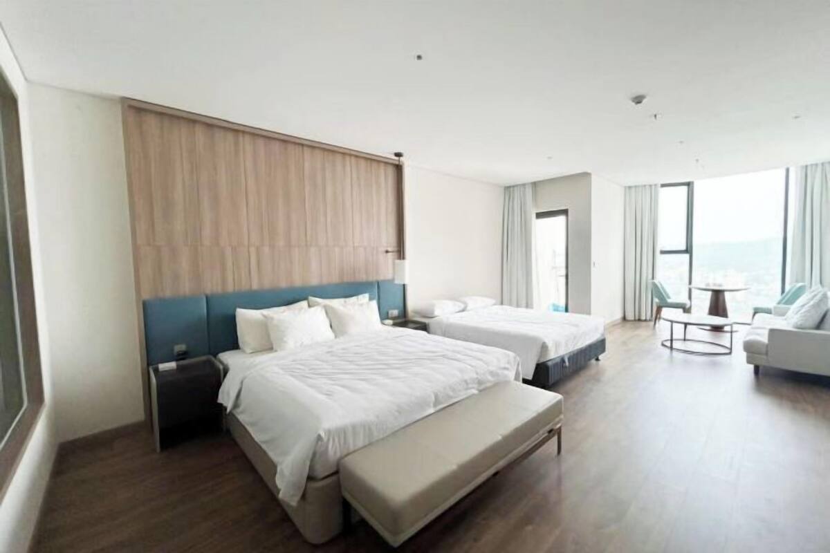 Een hotelkamer met twee bedden, een bankje, een kleine tafel en uitzicht op zee.