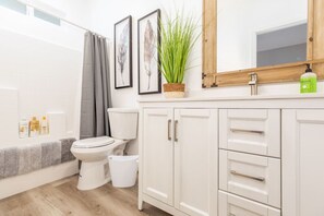 A bathroom with a toilet, a bidet, a sink with a mirror, and cabinets.
