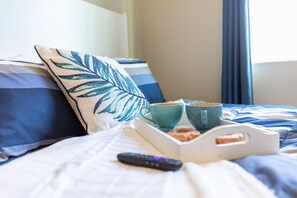 A neatly made bed with a pillow, a tray with pastries, two cups, and a remote control.