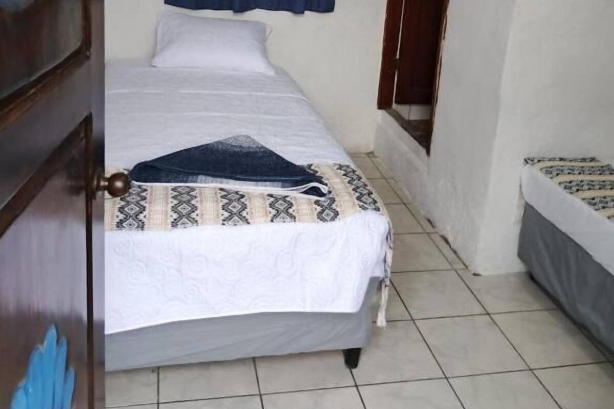 Ein Schlafzimmer mit einem Bett, einem Fenster mit blauen Vorhängen, einer Tür und einem gefliesten Boden.
