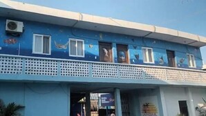 Un bâtiment à la façade bleue, doté de nombreuses fenêtres et d’un balcon avec un garde-corps ajouré.