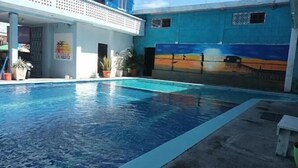 Une piscine avec une fresque murale sur le mur adjacent, des plantes en pot et un panneau indiquant l’emplacement d’un restaurant.