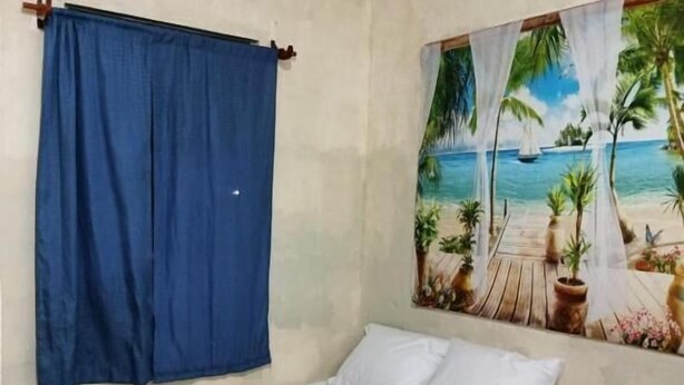Une petite pièce comprenant un lit, une table et une chaise. Un tableau représentant une scène de plage est accroché au mur.