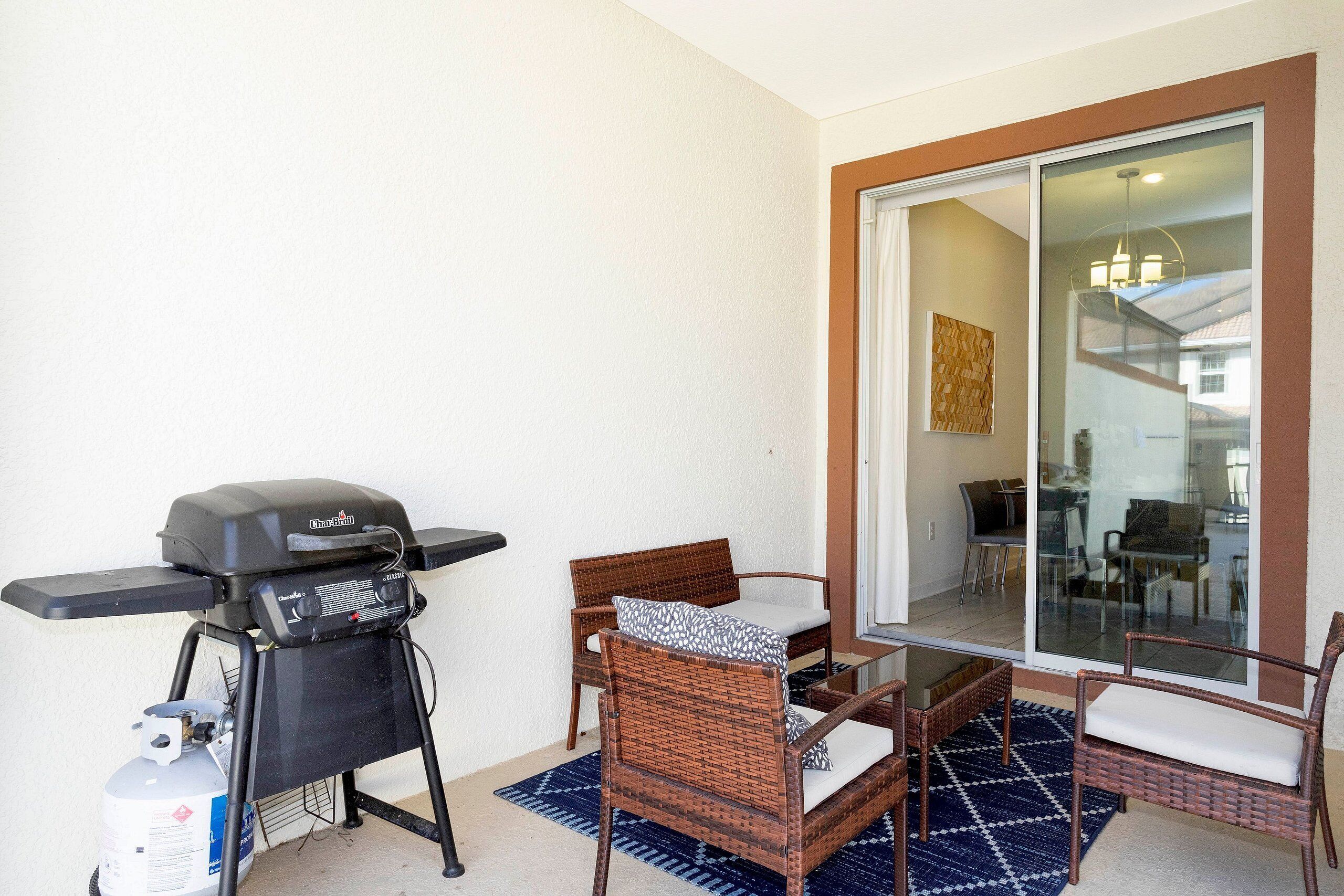 A patio with a grill, wicker chairs, a glass door leading to an indoor area, and a blue patterned rug.