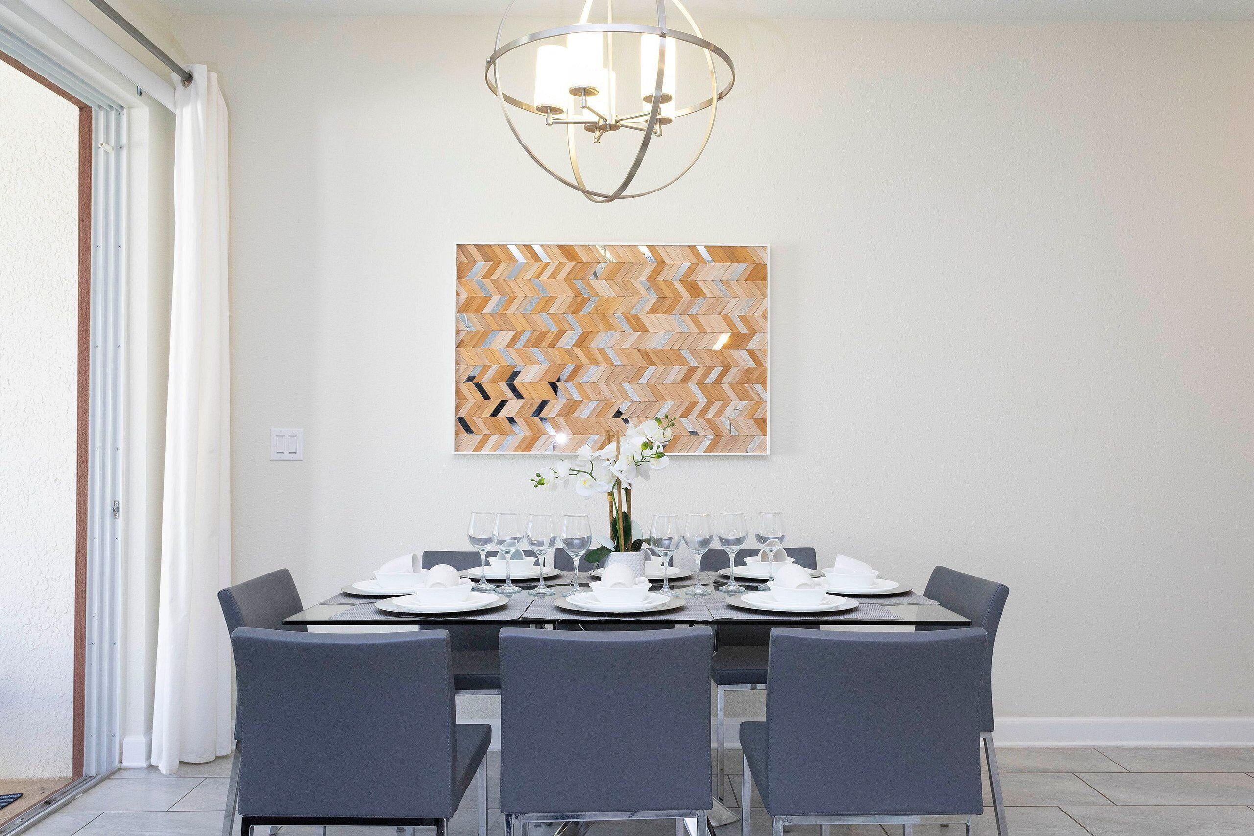 A dining area with a table set for six, a modern chandelier, and a geometric wall art piece.
