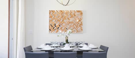 A dining area with a table set for six, a modern chandelier, and a geometric wall art piece.