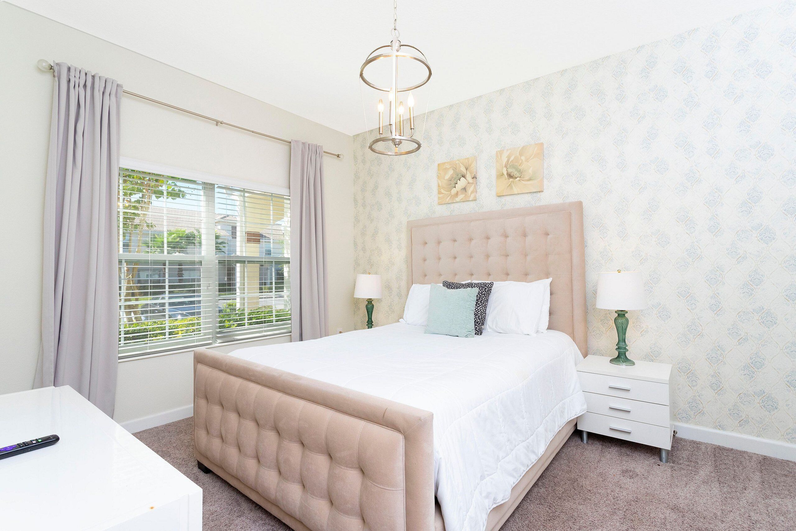 A bedroom with a large bed, a bedside table, a lamp, and a window with curtains.