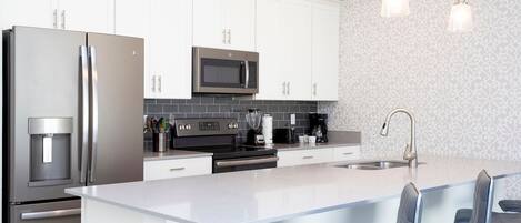A modern kitchen with stainless steel appliances, white cabinetry, a central island with bar stools, and pendant lighting.