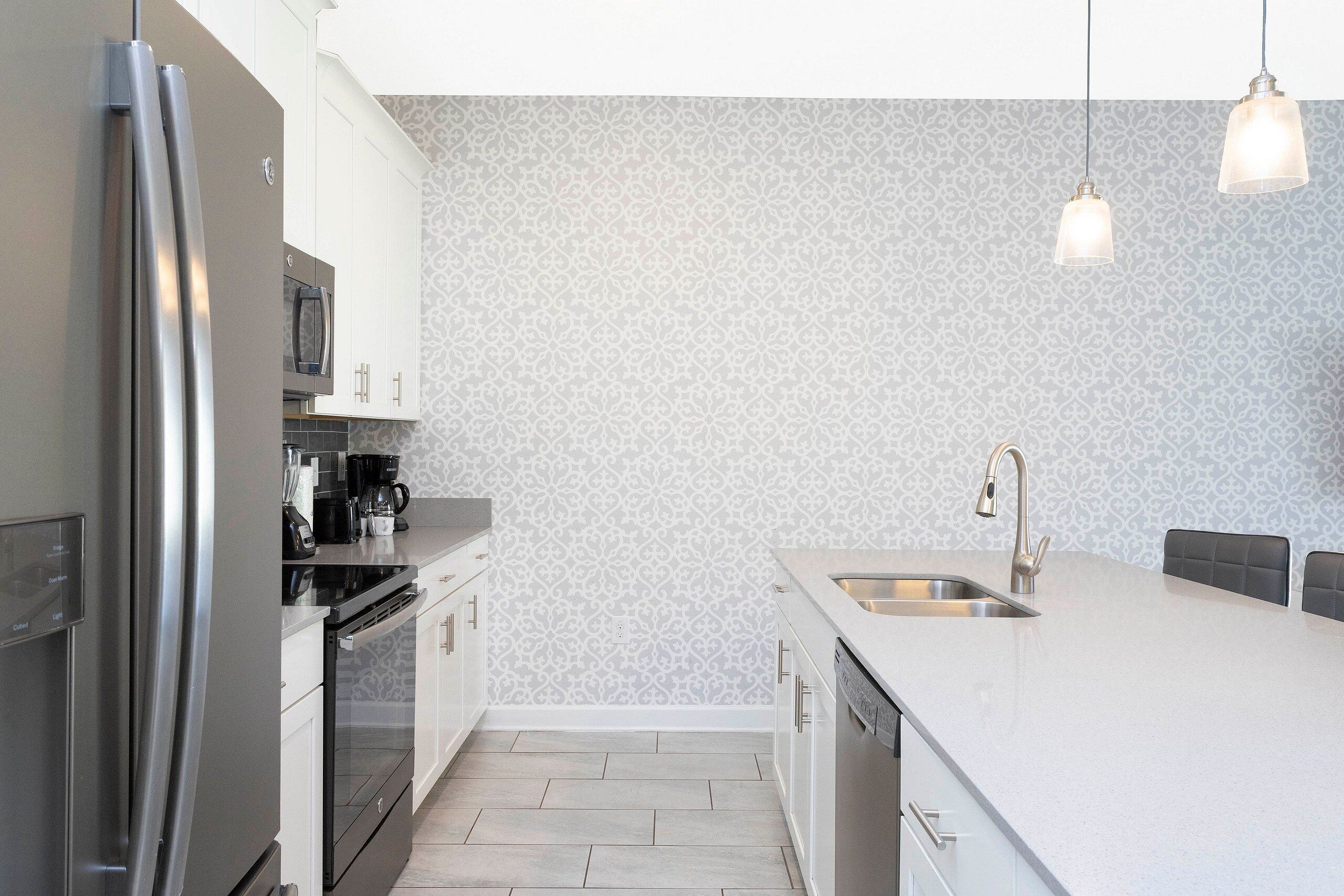 A modern kitchen with stainless steel appliances, a white countertop, and patterned wallpaper.