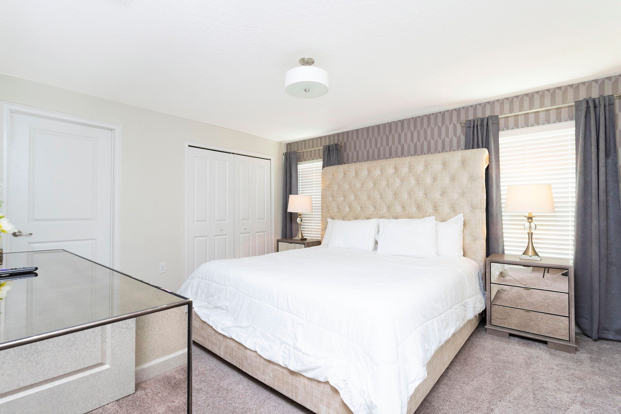 A neatly arranged bedroom with a large bed, bedside tables, and a glass desk.