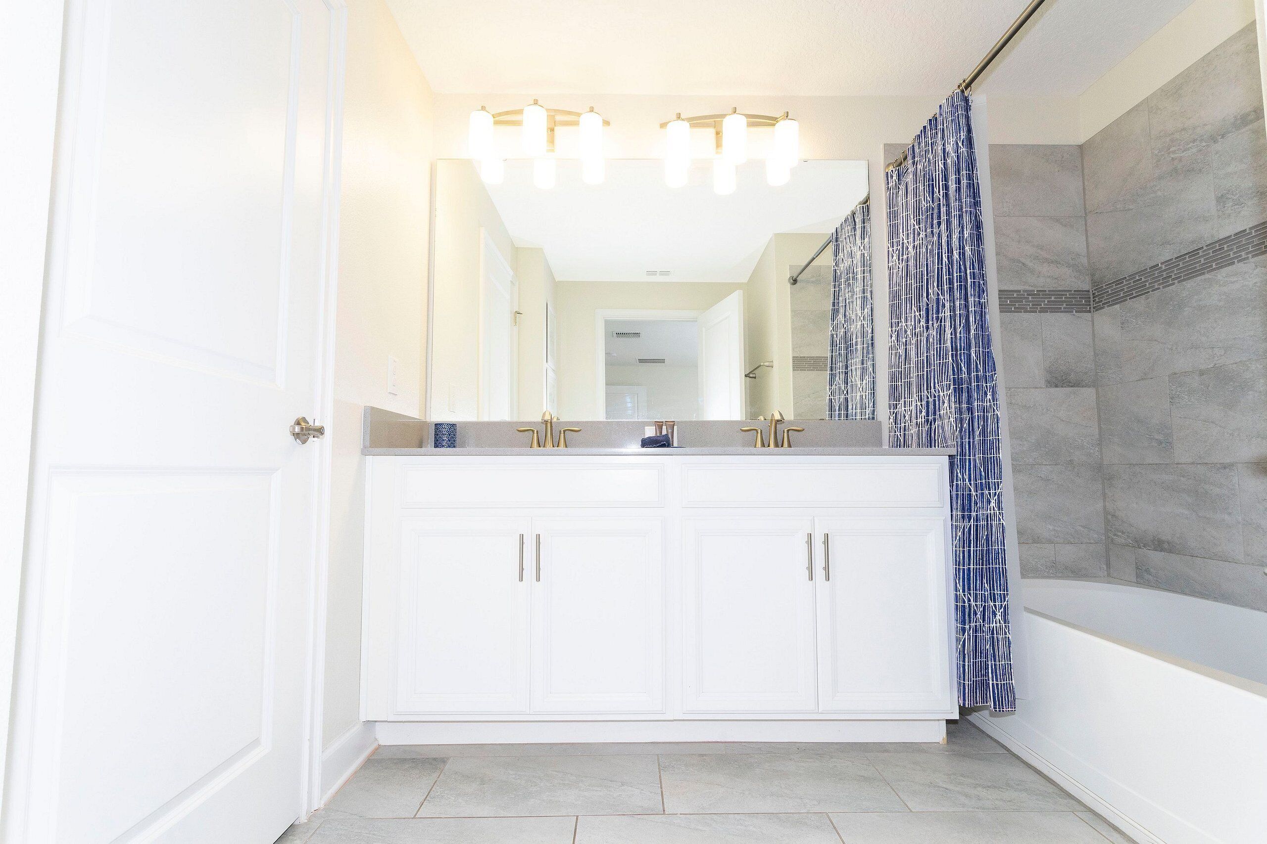 A modern bathroom with a double vanity, a shower with a patterned curtain, and a large mirror above the sink.