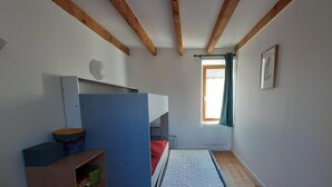 Une chambre avec un lit superposé, un petit bureau, une fenêtre avec des rideaux et un radiateur.