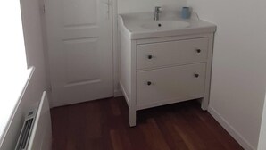Une salle de bain blanche avec un miroir rond, un lavabo et une porte.