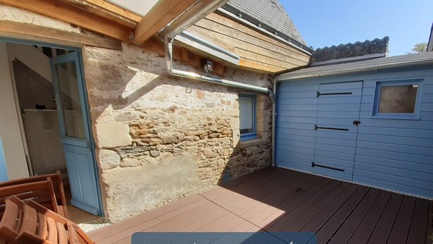 Un espace extérieur abrité doté d’une terrasse en bois, d’un mur en pierre et d’une porte de garage bleue.
