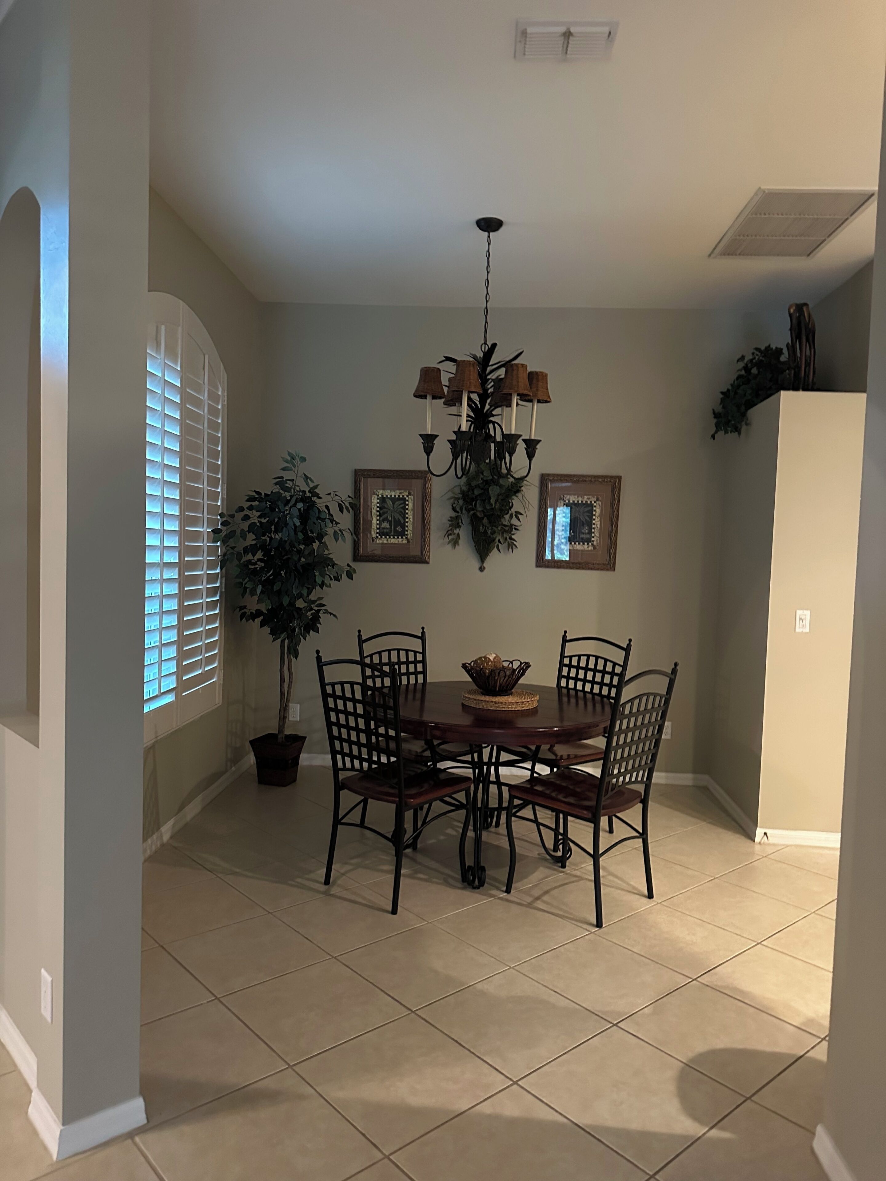 A dining area with a round table, six chairs, a chandelier, and two framed pictures on the wall.