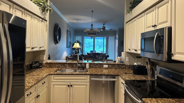 A modern kitchen with white cabinets, granite countertops, stainless steel appliances, and a dining area with a chandelier. - Coastal Comfort in the Heart of Naples (Naples)