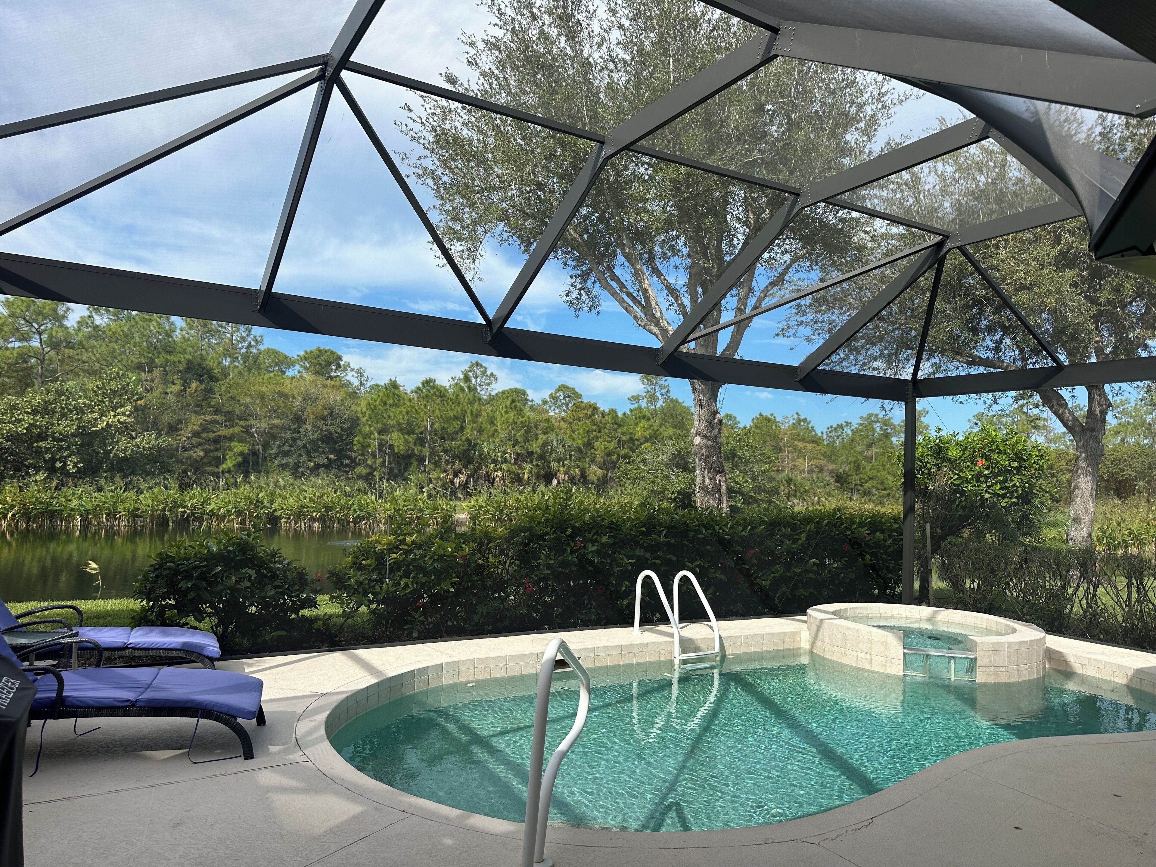 A covered outdoor swimming pool with a clear view of a lake and surrounding trees.