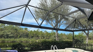 A covered outdoor swimming pool with a clear view of a lake and surrounding trees. - Coastal Comfort in the Heart of Naples (Naples)