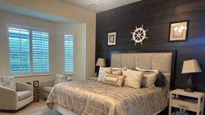 A bedroom with a large bed, two bedside tables, a chair, and a window with blinds. - Coastal Comfort in the Heart of Naples (Naples)