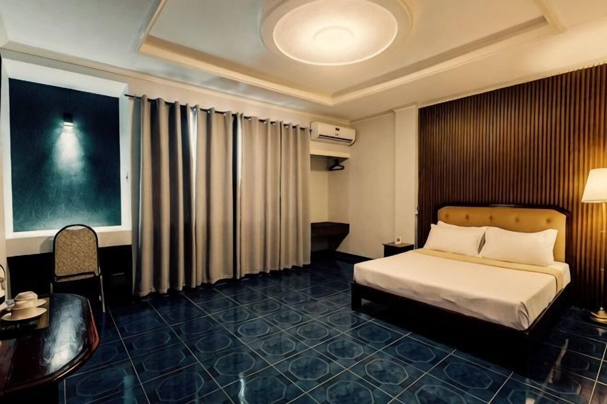 A hotel room with a bed, a desk, a chair, and a large window with curtains.
