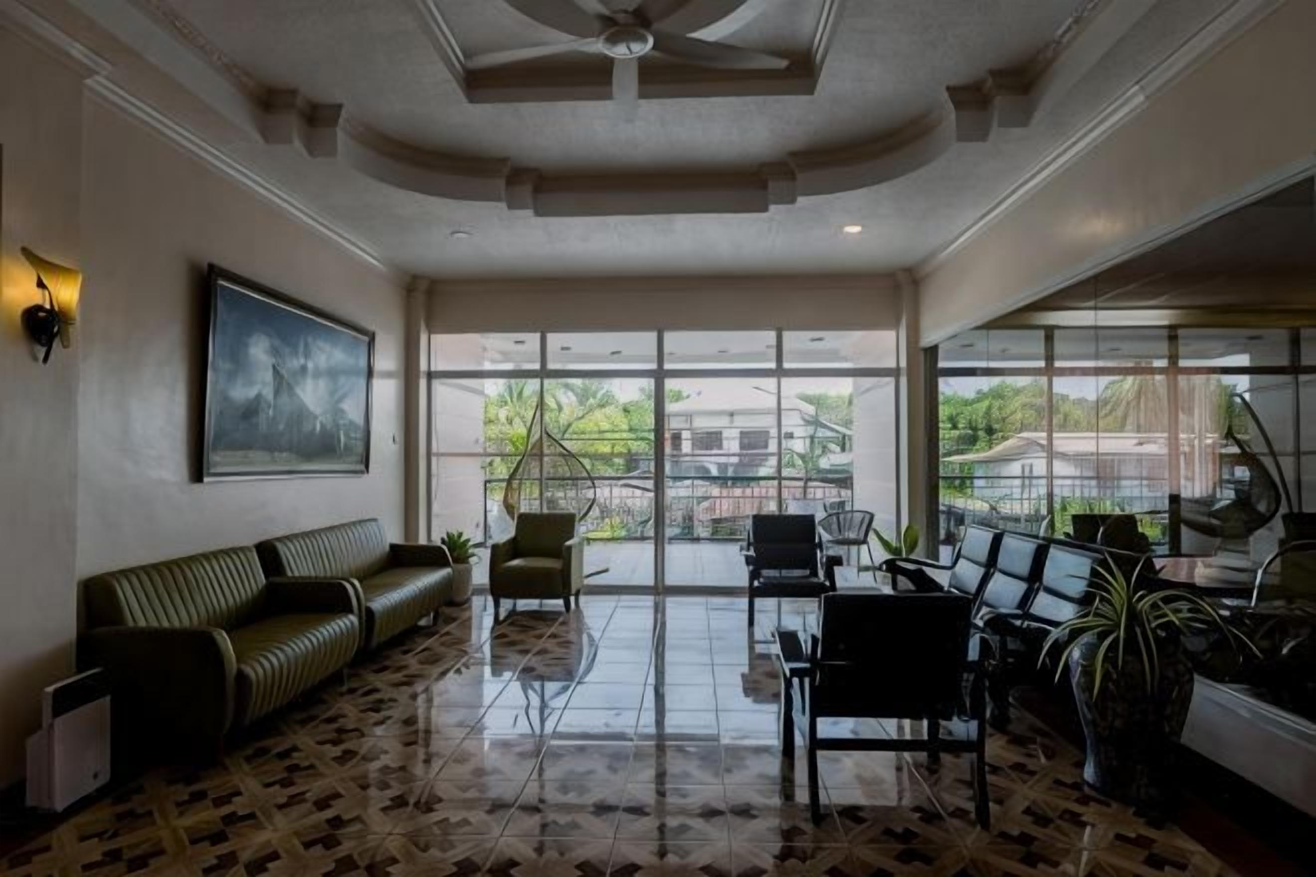 A spacious lobby with a high ceiling, a seating area with a sofa and chairs, and large windows offering a view of the outdoors.