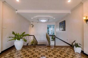 A hallway with a patterned floor, a staircase, and potted plants.