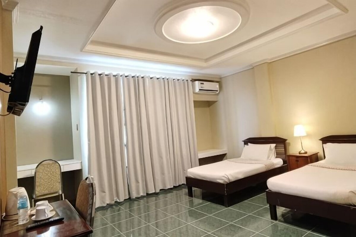 A hotel room with two beds, a desk with a chair, a TV mounted on the wall, and an air conditioning unit.
