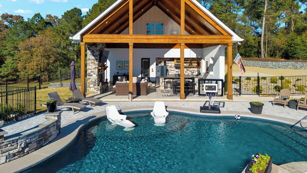 Une maison moderne avec une cheminée en pierre, une piscine avec un plongeoir et un patio couvert.