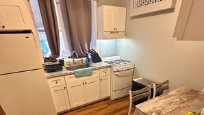 A compact kitchen with white cabinets, a stove, and a dining area with a table and chairs. - Fabulous studio apartment with AC in West New York (West New York)