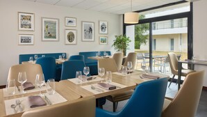 A restaurant with tables set for dining, blue chairs, and framed pictures on the wall.
