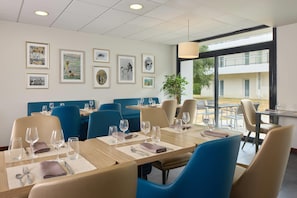 Un restaurant avec des tables dressées pour le service, des chaises bleues et des tableaux encadrés accrochés au mur.