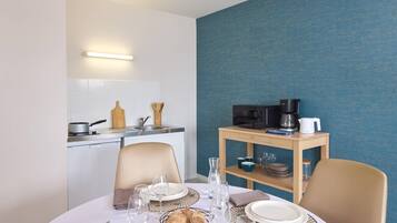 A dining area with a round table set for two, a kitchen in the background, and a blue textured wall.