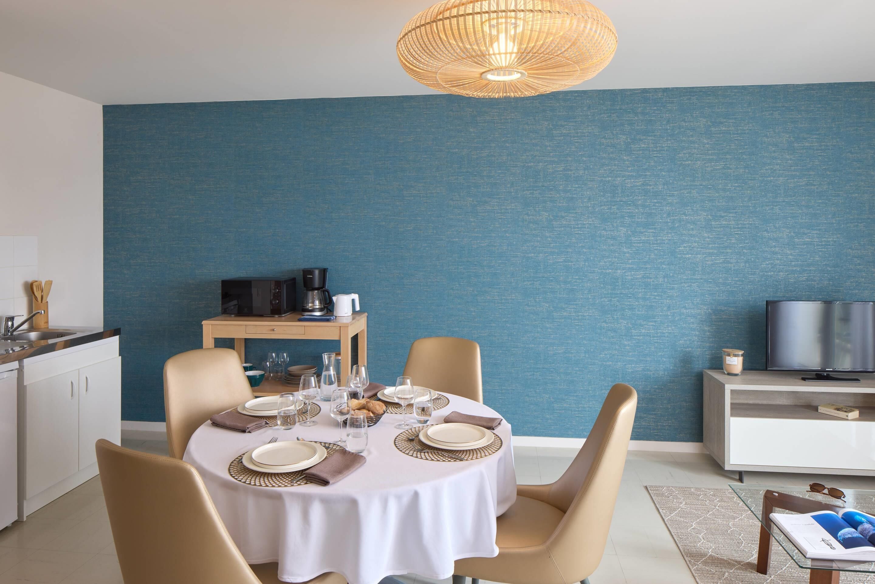 A dining area with a round table set for four, a television, and a coffee machine in the background.