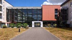 A modern building with a glass facade, a red accent wall, and a paved entrance. - Quality Aparthotel Portes de Rennes (Bruz)