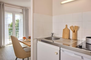 A modern kitchen with a sink, wooden utensils, and a dining area with a chair and table. - Quality Aparthotel Portes de Rennes (Bruz)