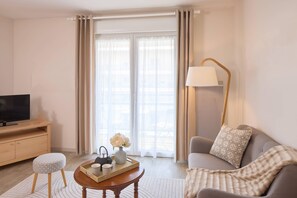 A modern living room with a television, a sofa, a coffee table, and a floor lamp. - Quality Aparthotel Portes de Rennes (Bruz)