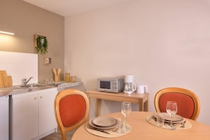 A clean, modern kitchen with white cabinets, a microwave, and a coffee maker. There is a dining table with chairs and a glass of water. - Quality Aparthotel Portes de Rennes (Bruz)