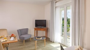 A hotel room with a bed, a desk with a laptop, a chair, a small table with a board game, a television on a stand, and a balcony with curtains. - Quality Aparthotel Portes de Rennes (Bruz)