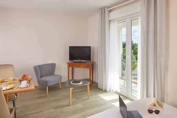 A hotel room with a bed, a desk with a laptop, a chair, a small table with a board game, a television on a stand, and a balcony with curtains. - Quality Aparthotel Portes de Rennes (Bruz)