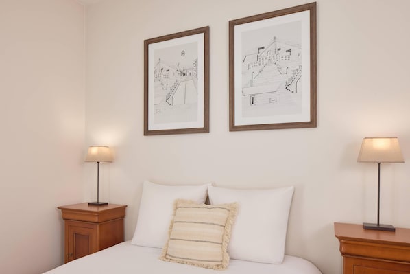 A neatly made bed with white linens and a striped pillow, flanked by two nightstands with lamps, and two framed black and white drawings on the wall. - Quality Aparthotel Portes de Rennes (Bruz)