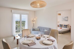 Een eetgedeelte met een ronde tafel voor vier personen, een bank en een bed op de achtergrond.