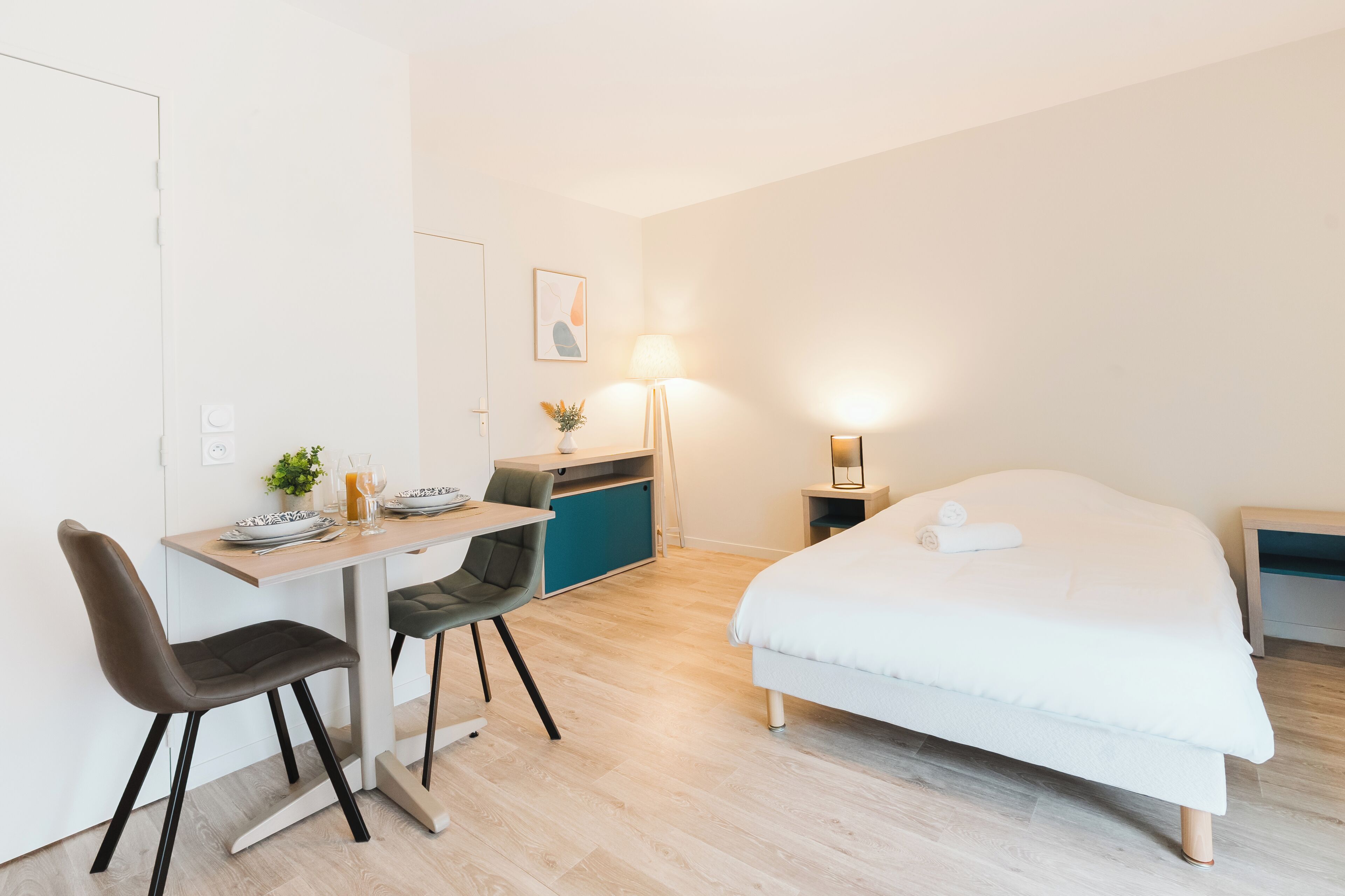 Une chambre d’hôtel moderne équipée d’un lit, d’un bureau, de chaises et d’une petite kitchenette.