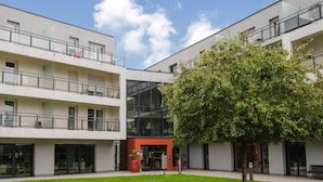 Un bâtiment moderne doté de nombreux balcons, de grandes fenêtres et d’une cour intérieure avec un arbre.