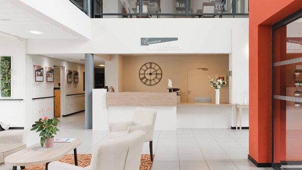 Un hall d’hôtel moderne comprenant un comptoir d’accueil, un espace salon et un escalier menant à un étage supérieur.