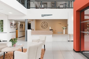 Un moderno vestíbulo de hotel con mostrador de recepción, zona de estar y una escalera que lleva a un nivel superior.